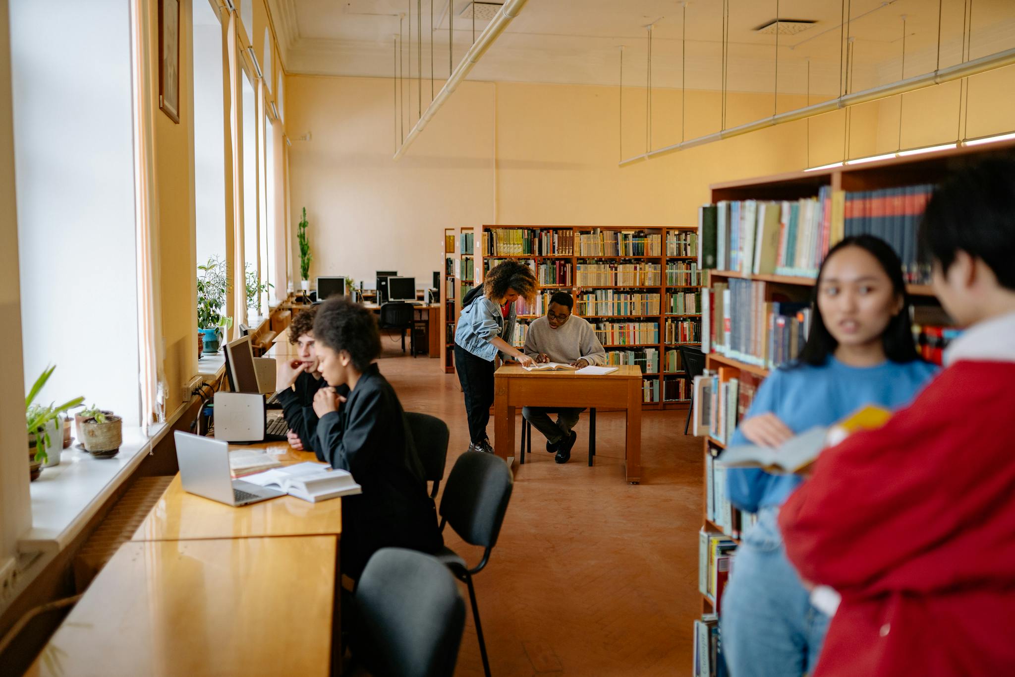 Students studying and collaborating in a university library setting with bookshelves and desks.
