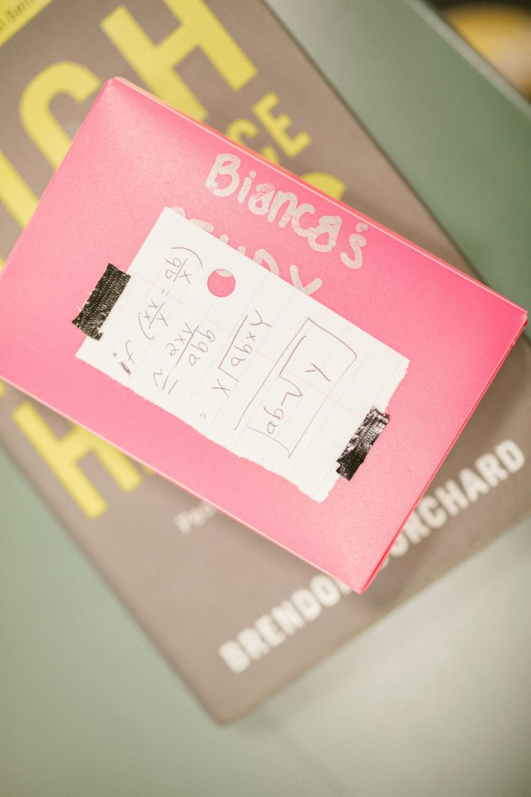 Top view of a mathematics cheat sheet taped to a pink box, resting on educational books.