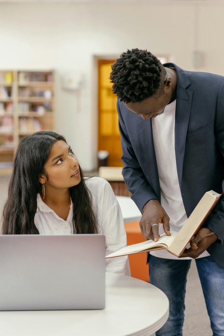Young adults engaging in a focused study session with books and laptops in the library.